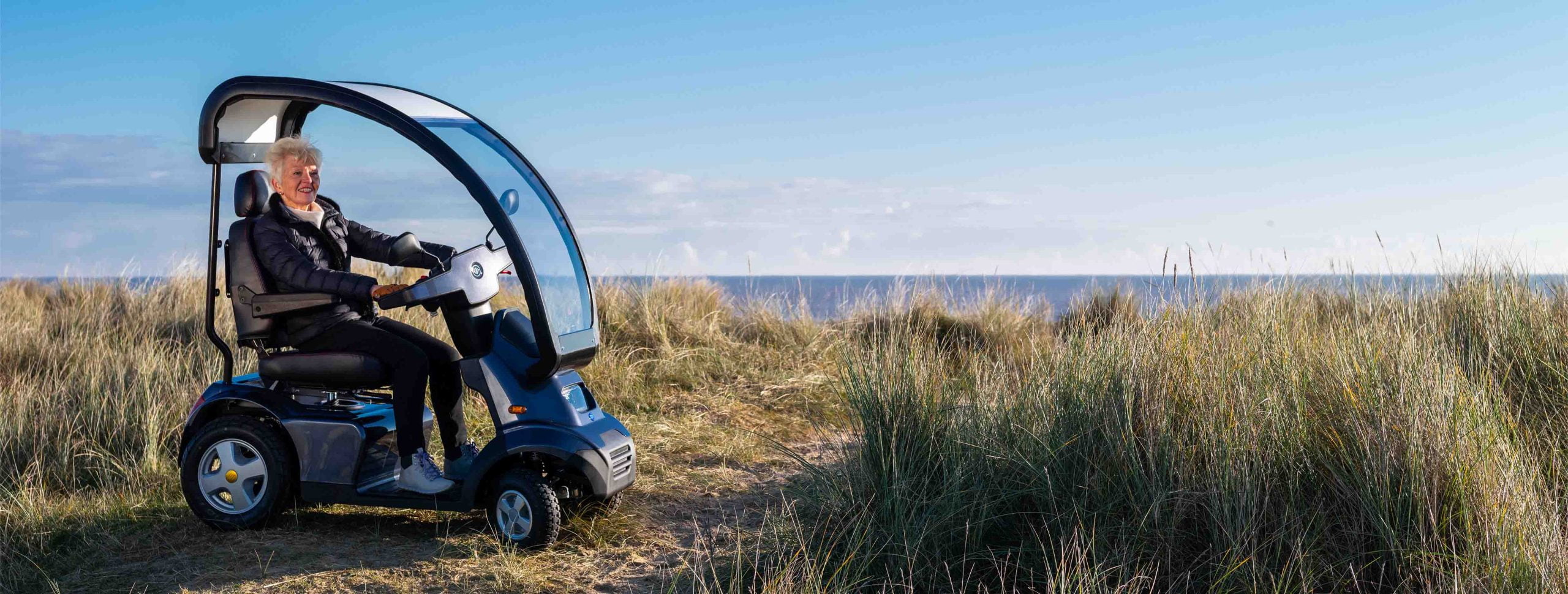 A person using a mobility scooter with a canopy on a beach by the sea