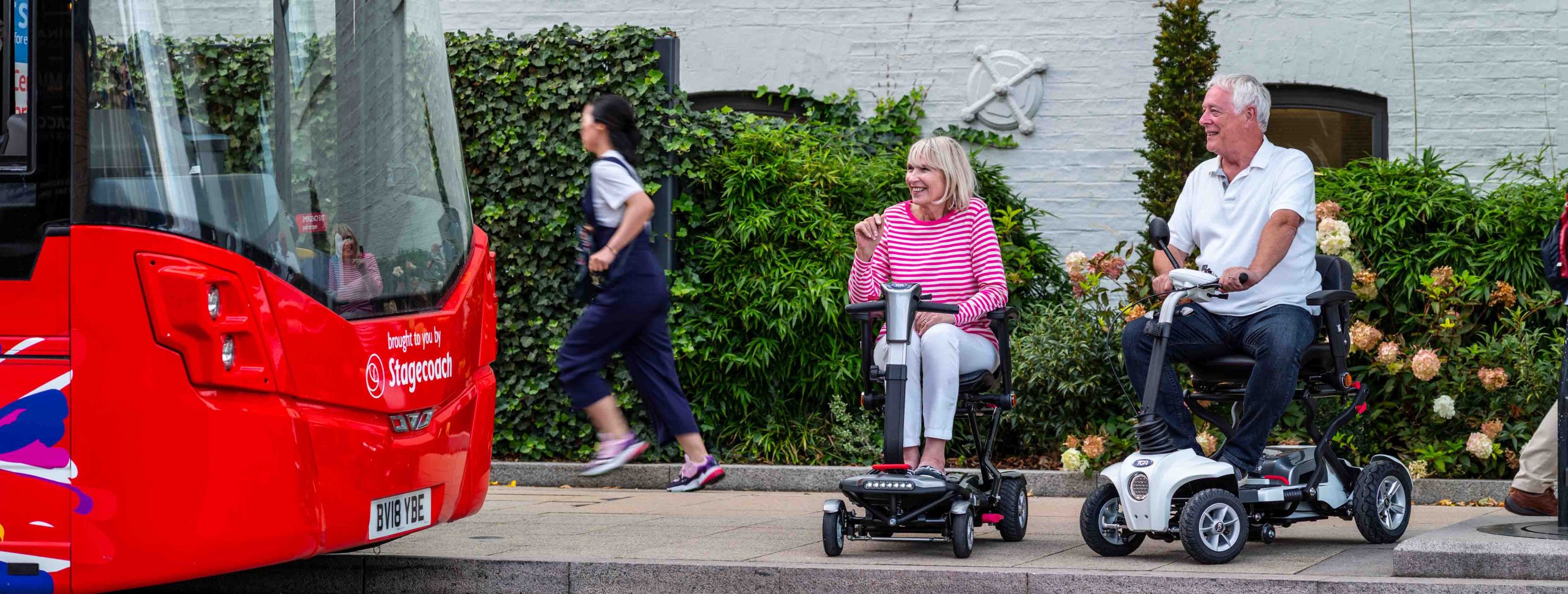 A man and a woman on mobility scooters waiting for a bus