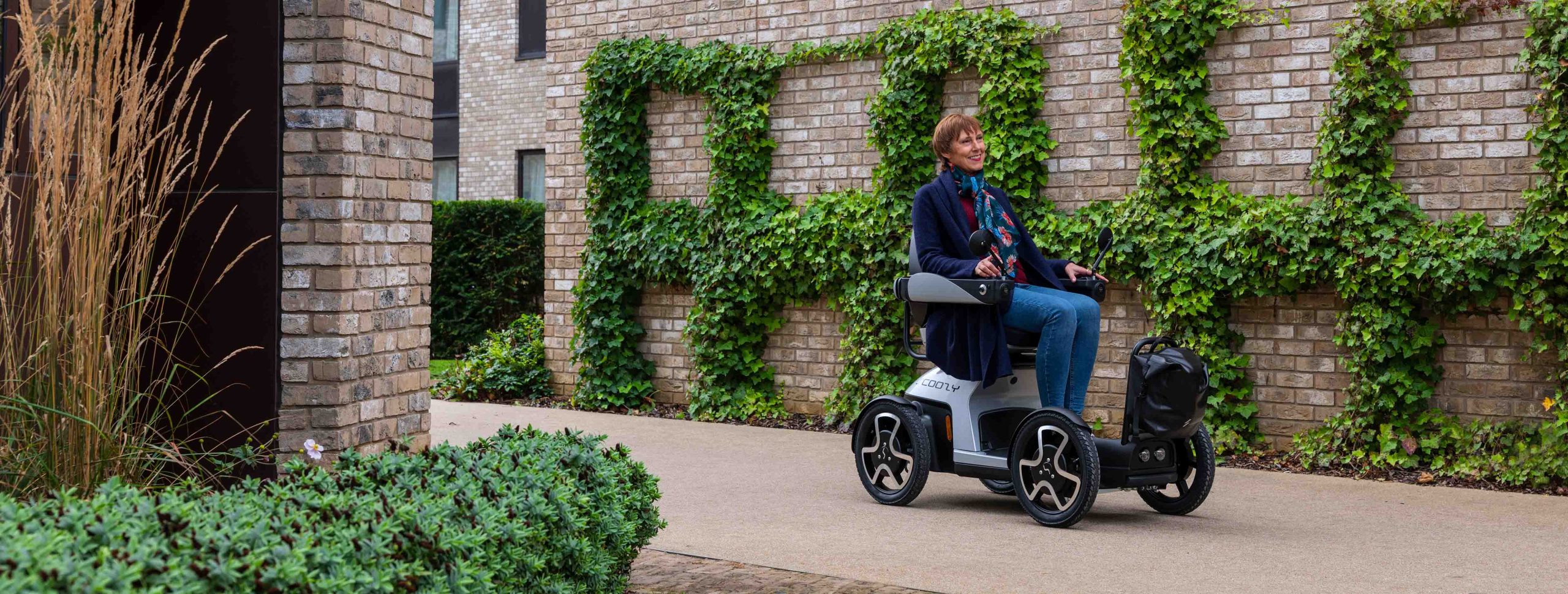 off road scoozy powerchair with a lady on, with a scenic green background