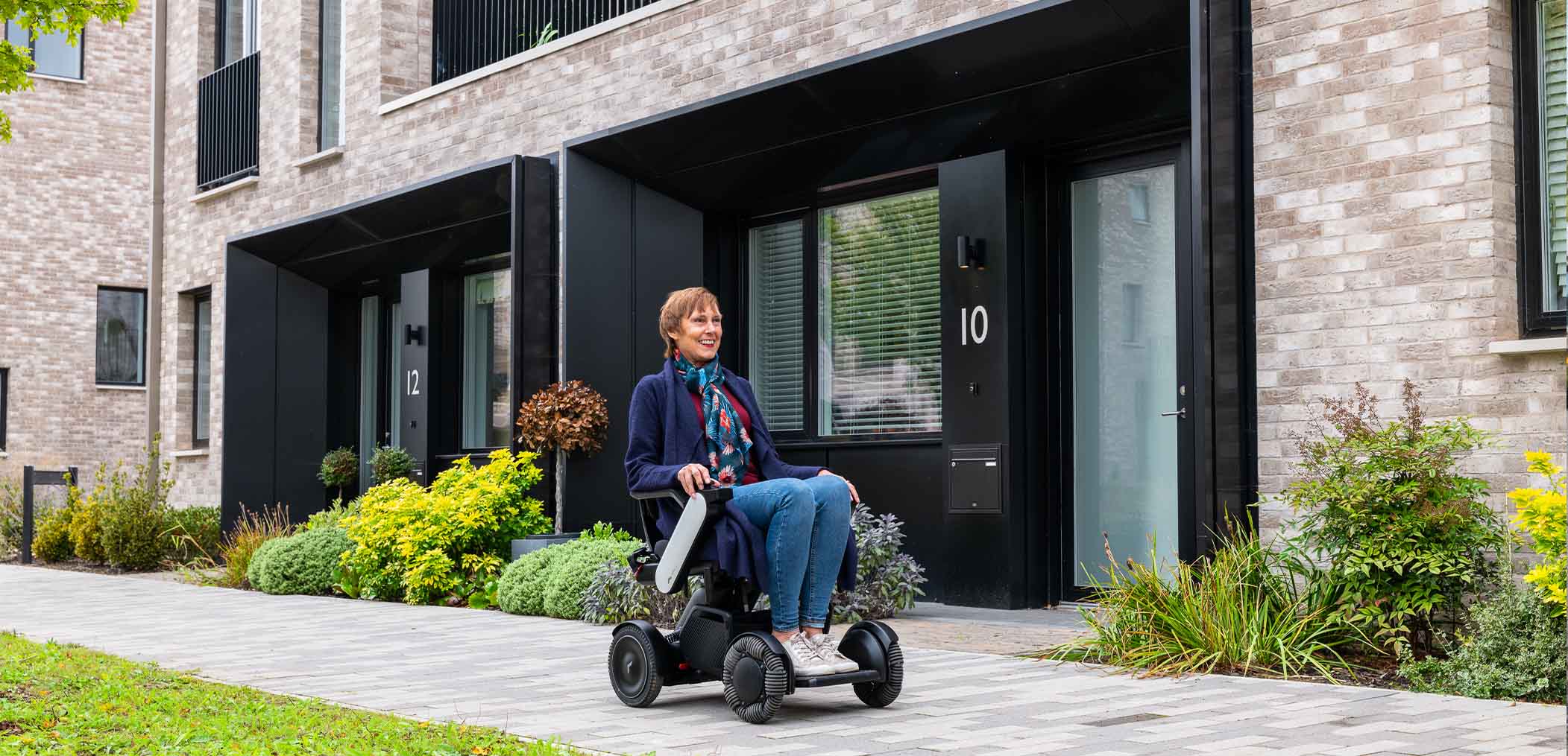 Woman in a Whill C2 strolling past housing with green plants
